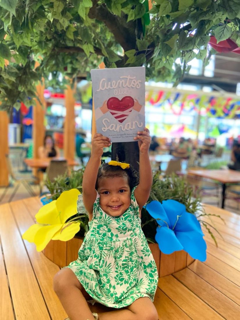 Niña levanta feliz el libro Cuentos que Sanan