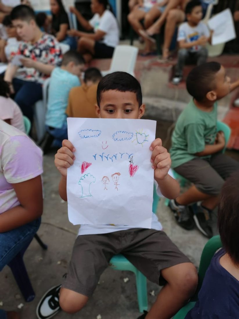 Niño muestra su dibujo de corazones y árboles