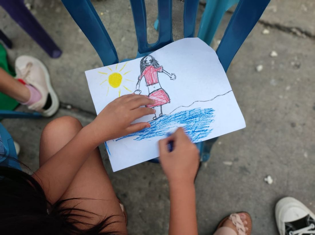 Niña colorea un dibujo con sol y mar