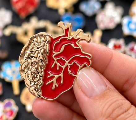Pin de cerebro y corazón sostenido en la mano, con más pines al fondo
